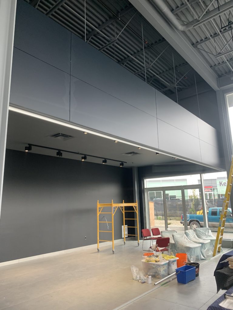 Poplar Painting - A modern, under-construction interior with gray walls, an exposed ceiling, and a partially concealed hvac duct. a ladder, a scaffold, and various construction materials are scattered around the space.