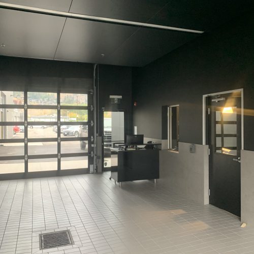 Poplar Painting - An empty modern commercial space with black walls and ceilings, featuring a reception desk and doors, illuminated by natural light from the entrance.